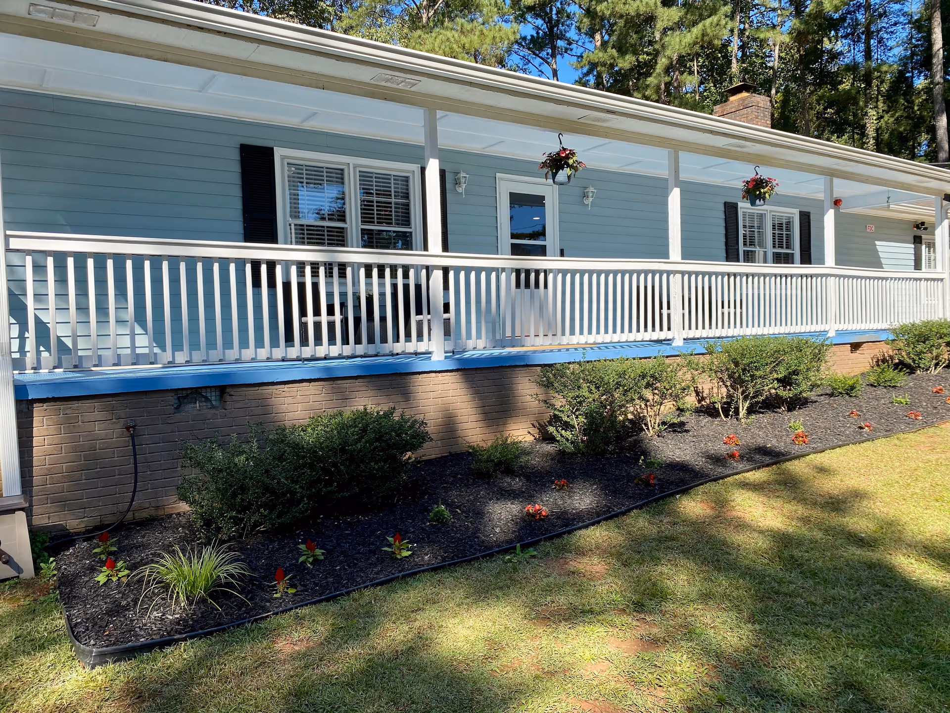 Blue single-story building with a long white railing porch, hanging baskets, and landscaped front yard.