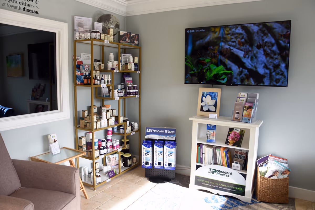 Waiting area with medicine shelves, a mounted TV, and a magazine stand in a care facility.