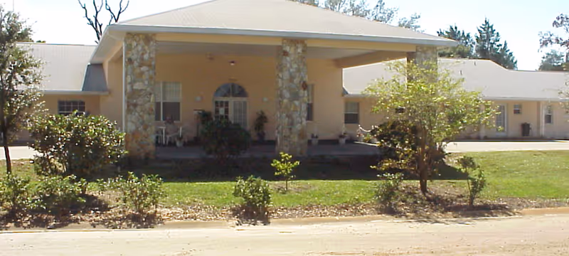Single-story senior living facility with a front porch, stone columns, and manicured landscaping.
