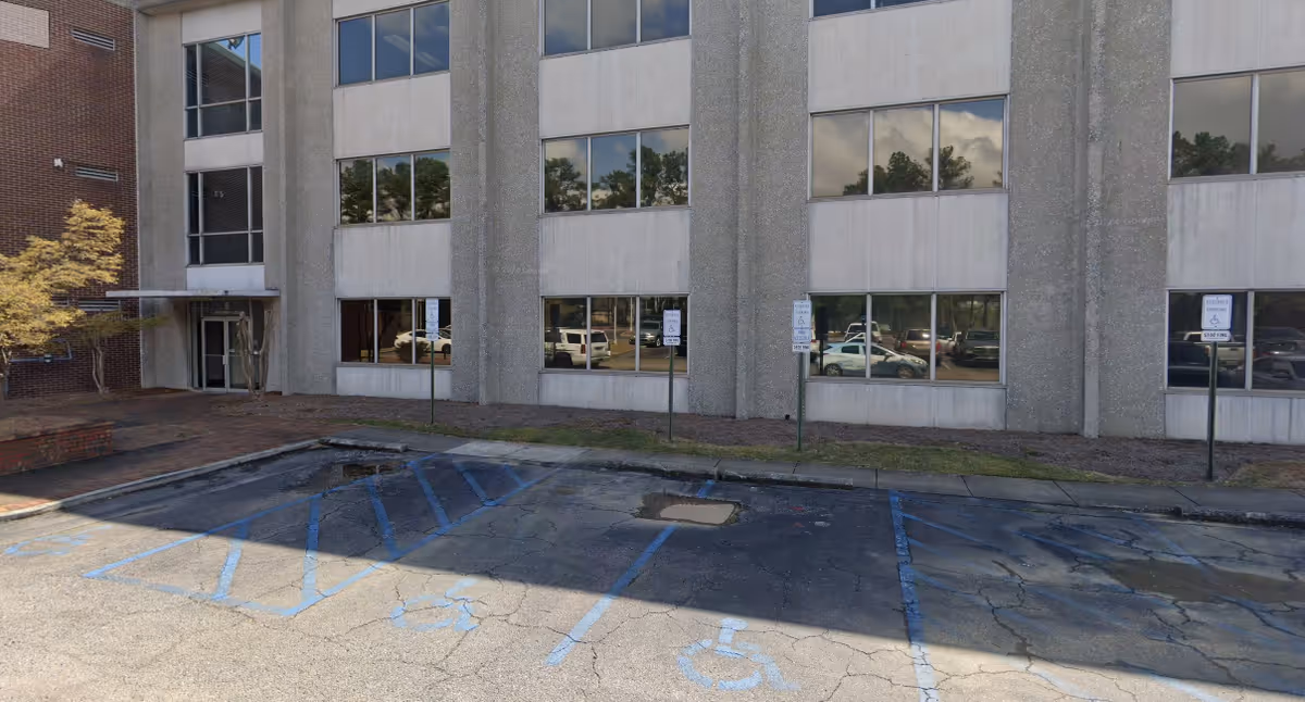 Exterior view of a concrete-office building with blue handicap parking spaces in front.