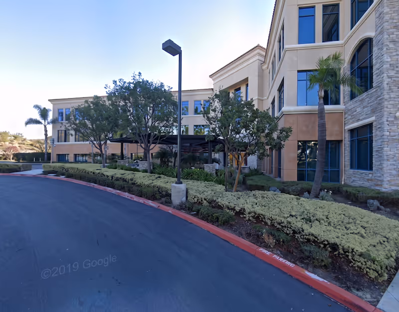 A multi-story senior living facility exterior with landscaping, a curved driveway, and tall windows.