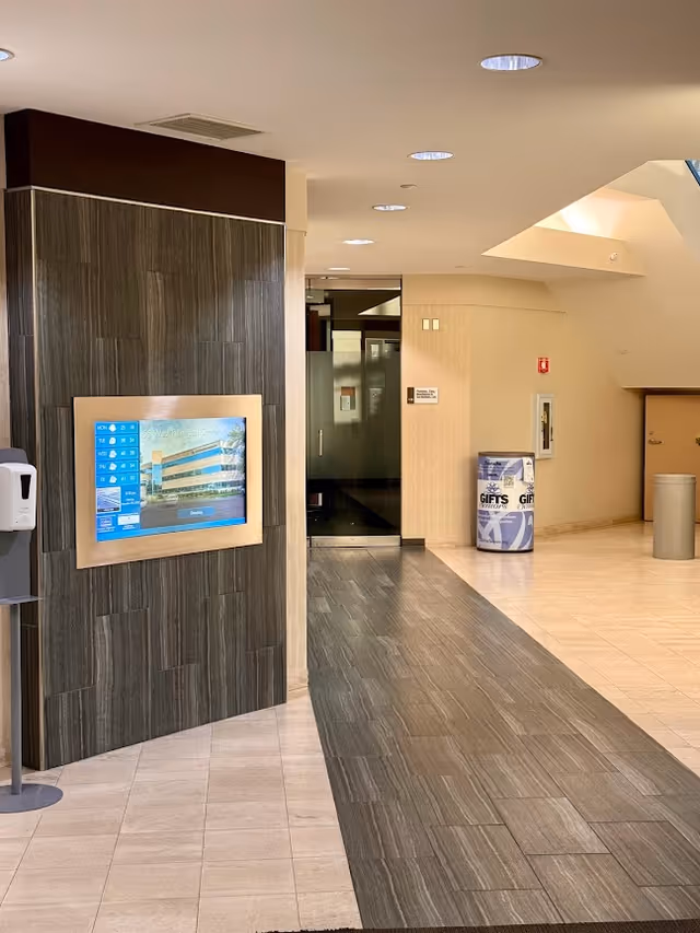 Hotel-like senior living lobby with display screen, elevators, and tiled corridors.