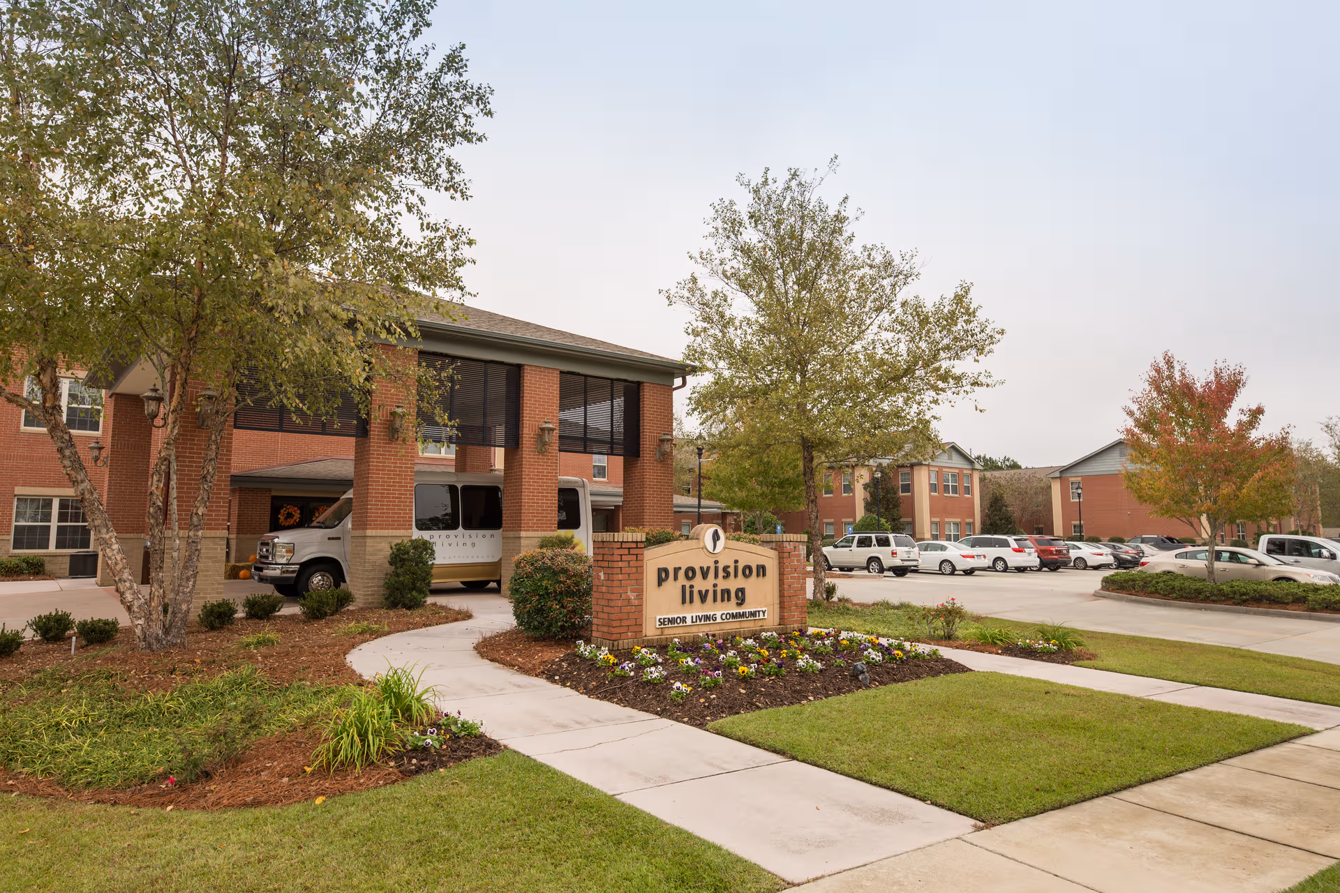 Brick senior living facility exterior with front entrance, sign, and parked cars.