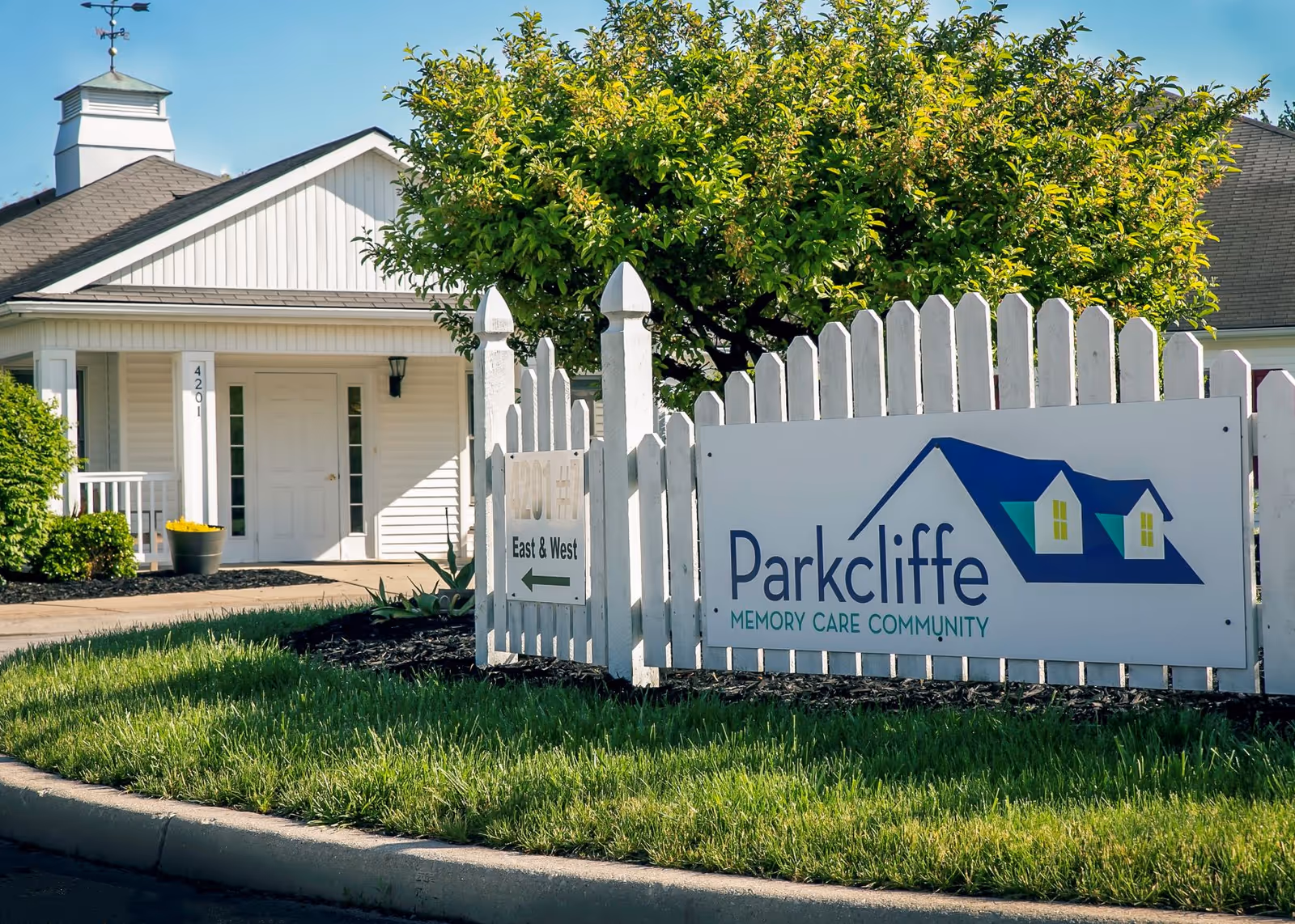 White building with a white picket fence and Parkcliffe Memory Care Community sign.