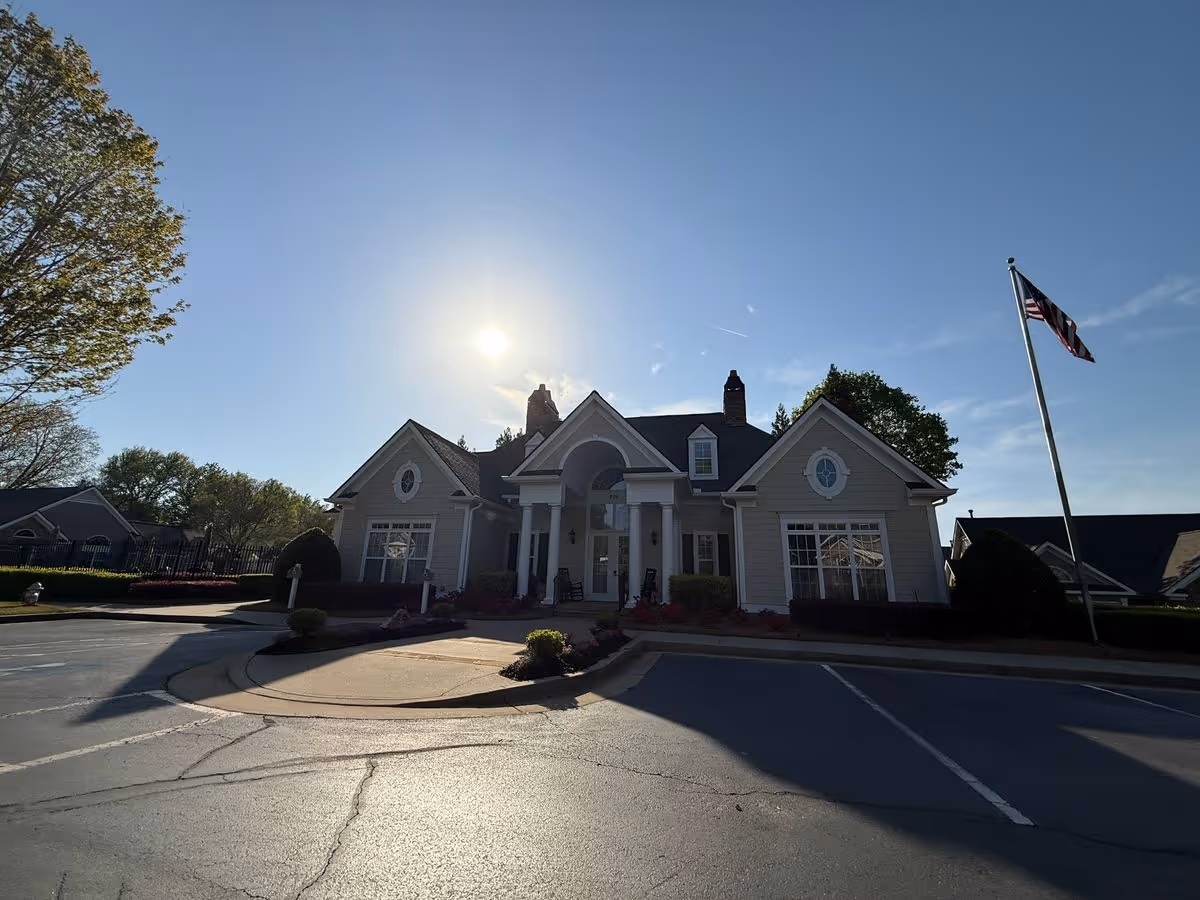 Low-angle view of a clubhouse-style single-story building with columns and an American flagpole in front under a bright sky.