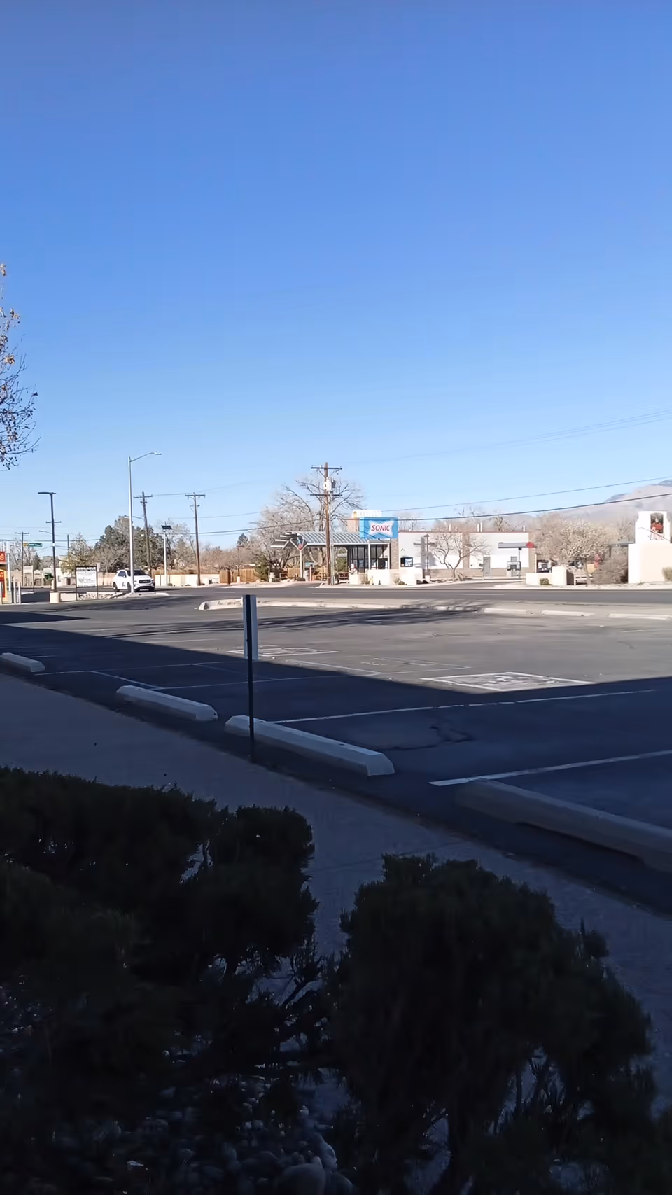 Bright blue sky over a large parking lot with distant storefronts along a street.