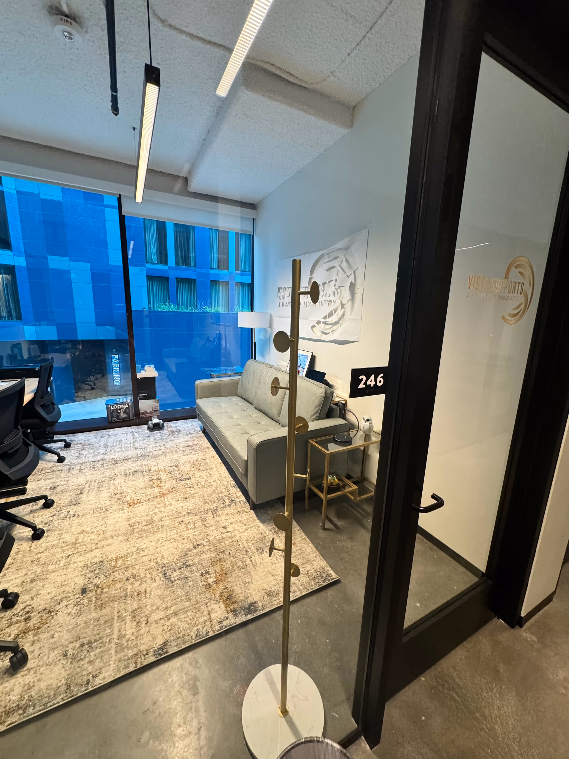 Modern office-like lounge inside Vista Supports with sofa, glass walls, and a desk area.