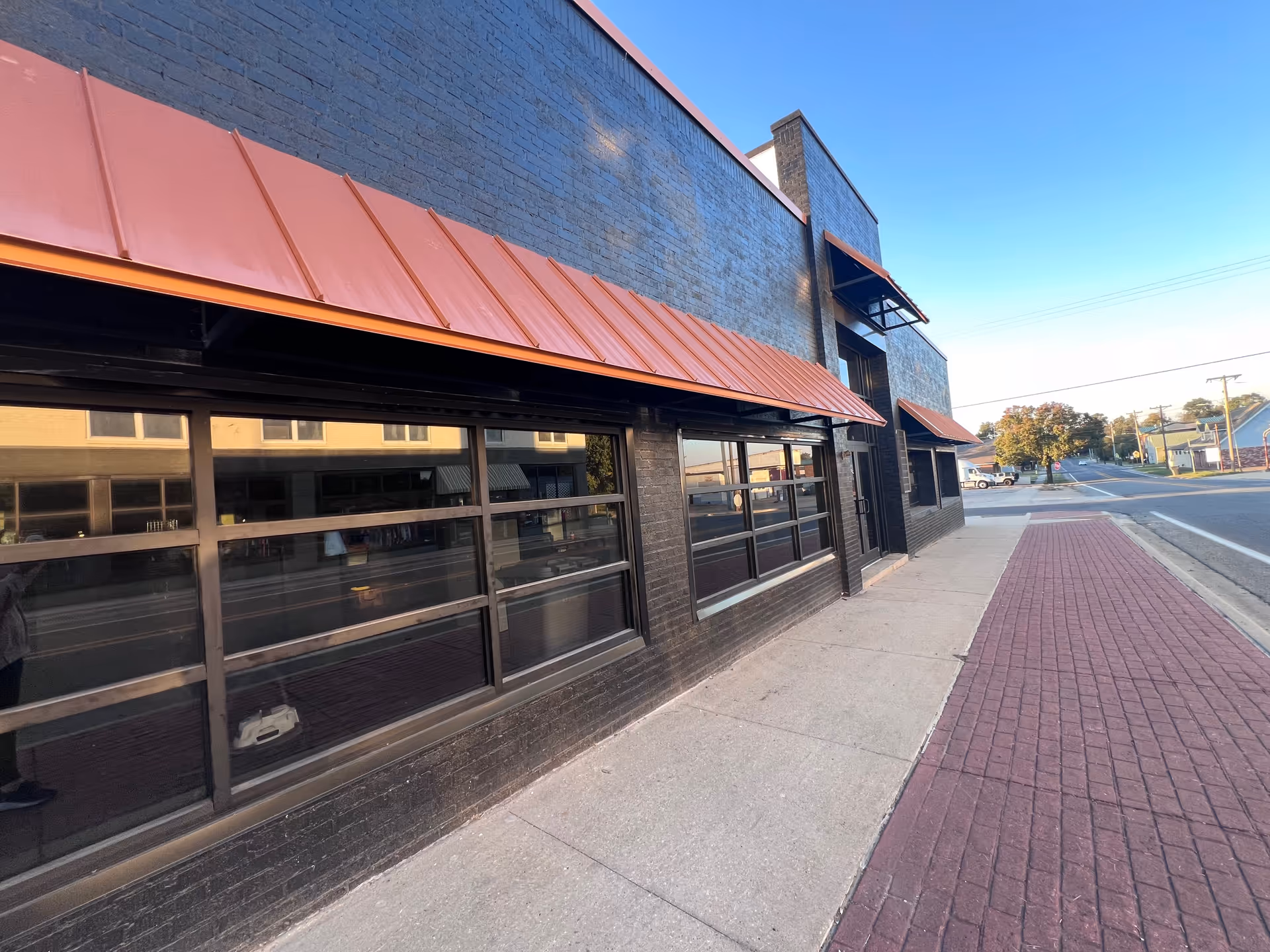 Exterior view of a brick building with large windows and red awnings along a sidewalk.