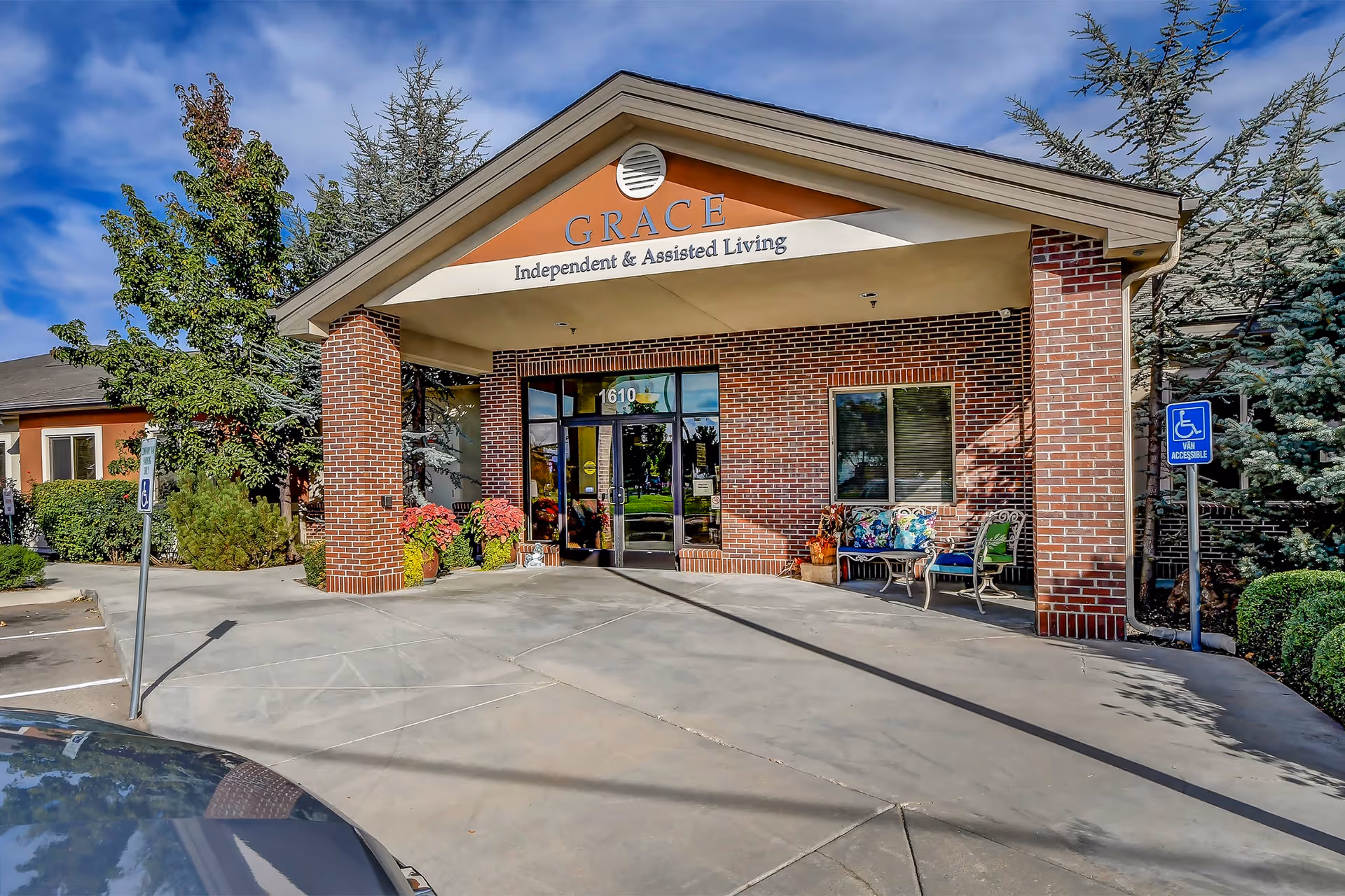 Front entrance of Grace Assisted Living showing a covered brick portico with signage, glass doors, and accessible parking.