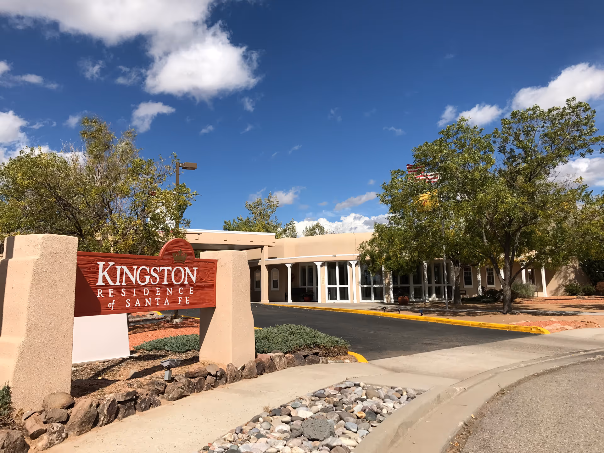Front exterior of Kingston Residence of Santa Fe with sign, driveway, and trees under blue sky.