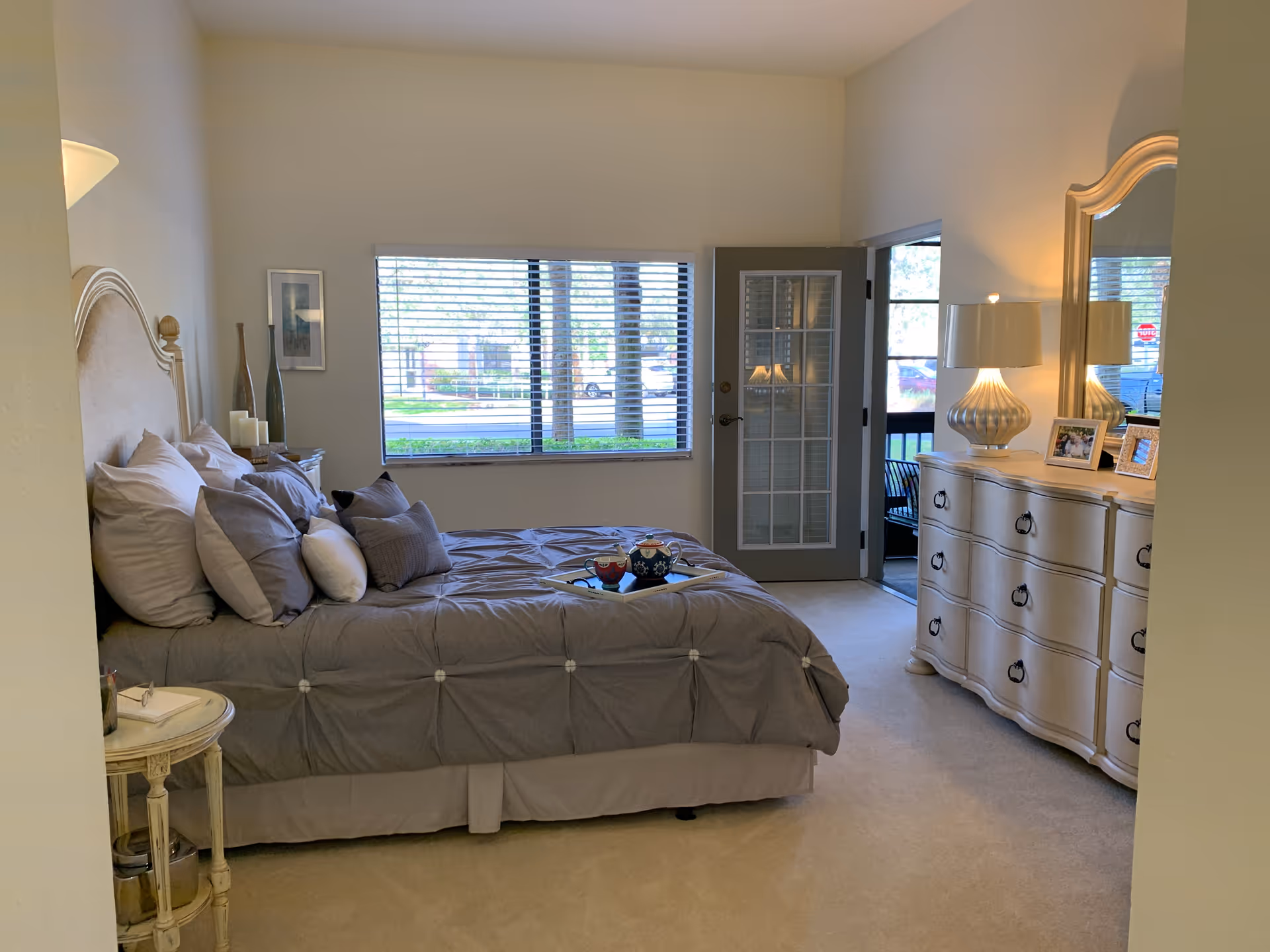 Cozy bedroom with a large bed, dresser, nightstand, window blinds, and French door.