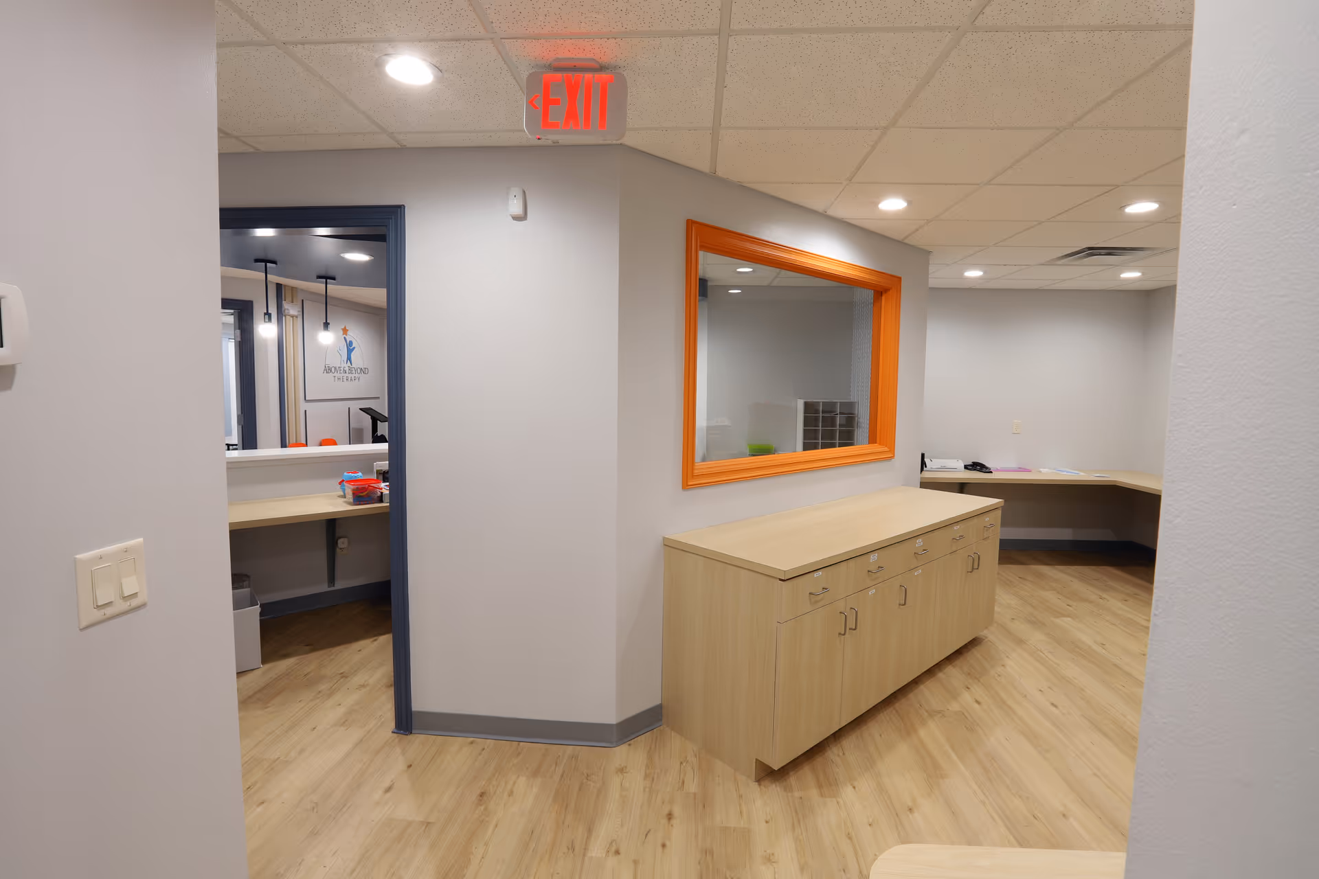 Bright interior hallway with wooden cabinetry and an orange-framed window inside a senior facility.