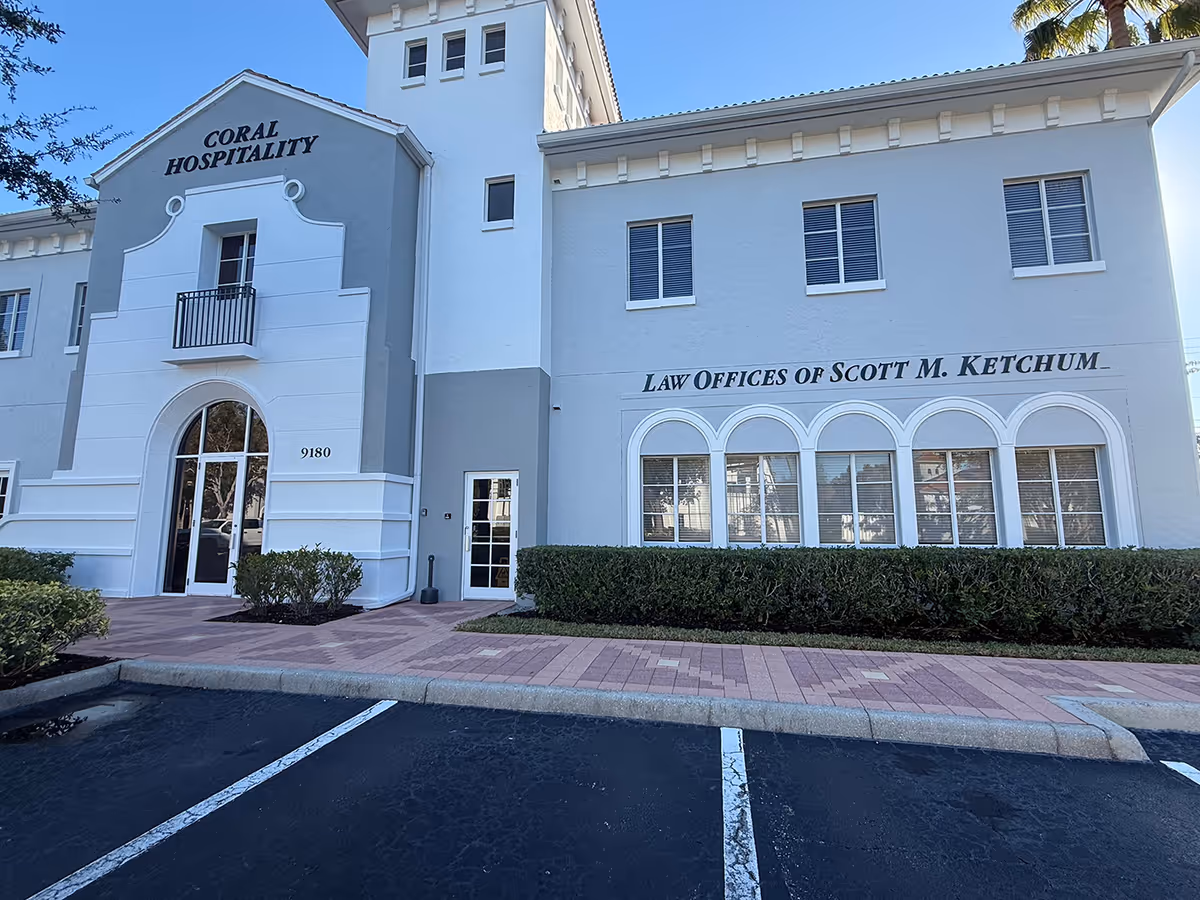 White multi-story building exterior with arched windows and signage, parking lot in foreground.