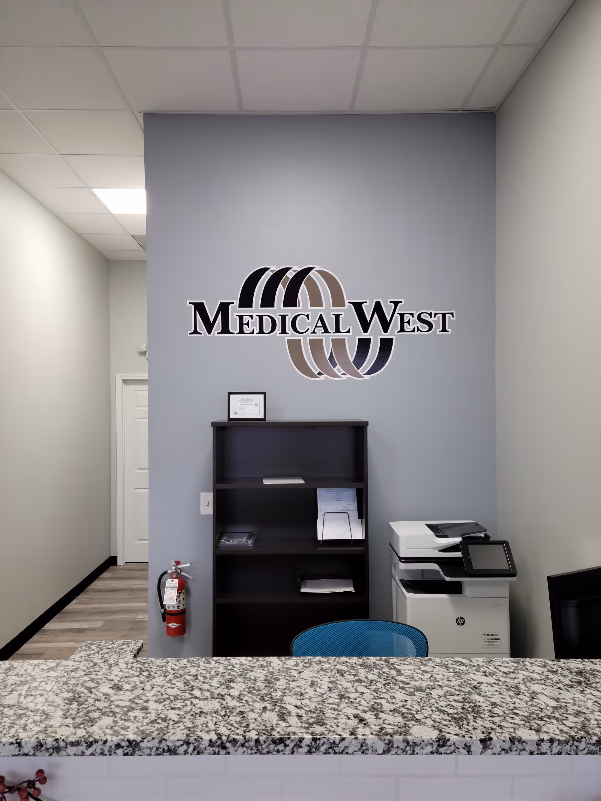 Registration counter in a Medical West facility with logo on wall and office equipment.