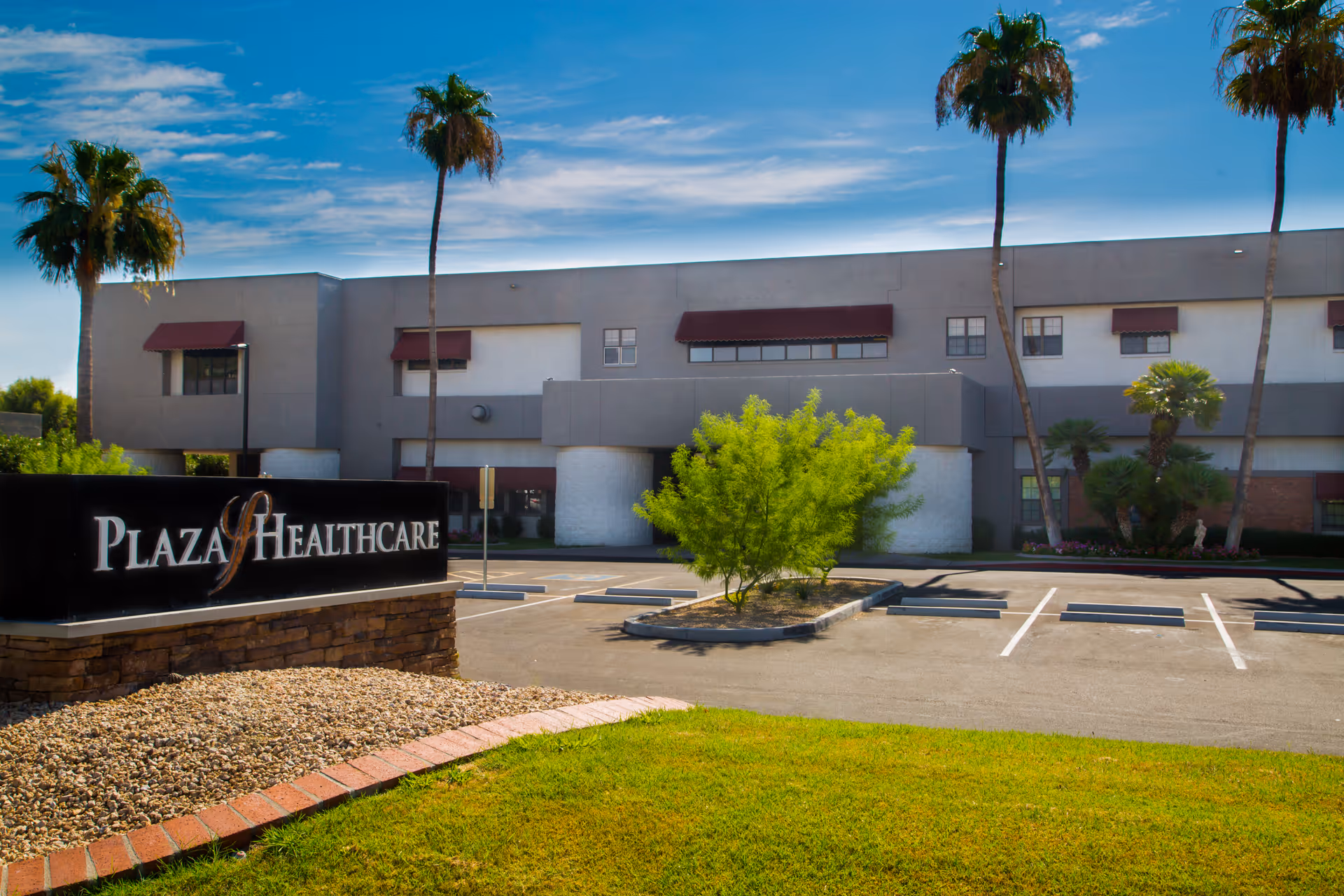 Exterior view of Plaza Healthcare building with a parking lot in front, palm trees, and a clear blue sky.