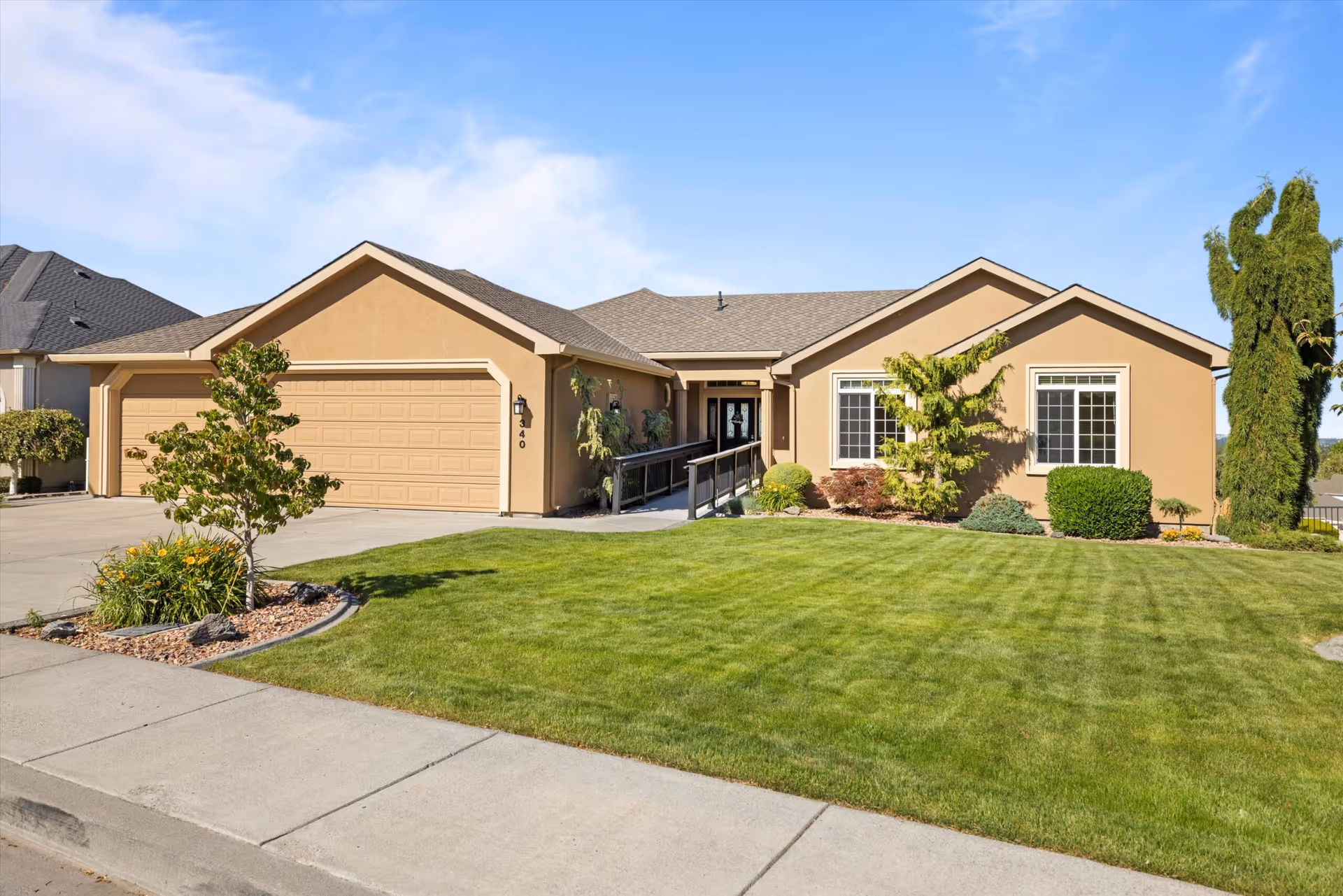 A single-story tan house with a two-car garage and a well-maintained front lawn.