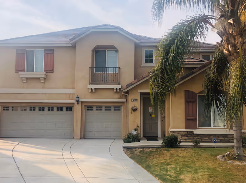 Beige two-story building with two garages, an entry door, and a palm tree.