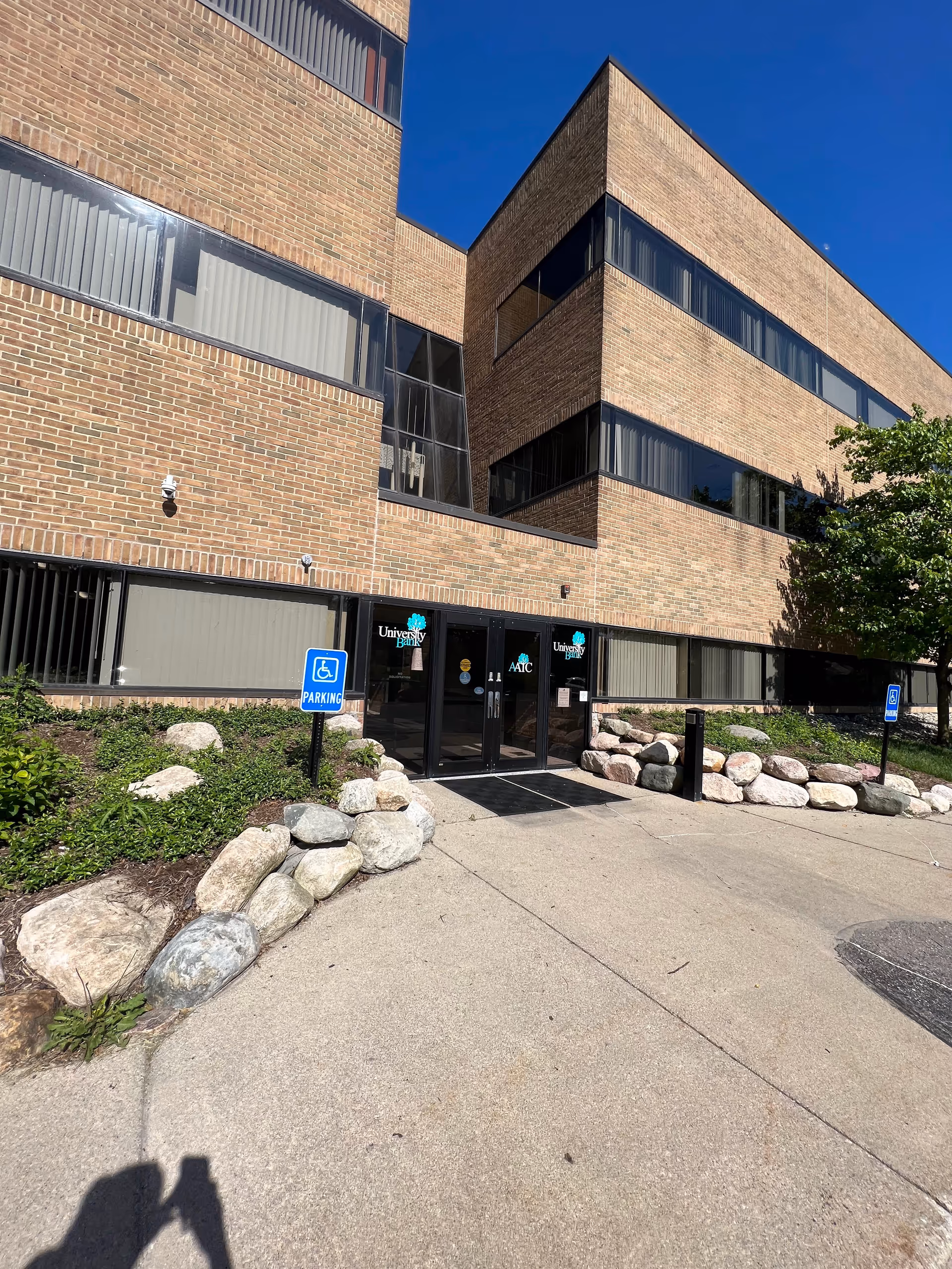 Exterior brick building entrance with glass doors, sidewalk, rocks, and handicap parking signs.