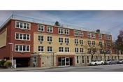 Exterior view of Little Neck Care Center, a multi-story building with ground-floor storefronts and parked cars.