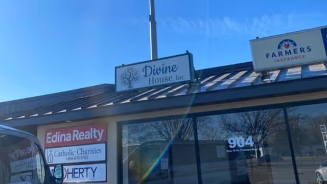 Exterior view of Divine House, Inc., storefront with realty and insurance signs.