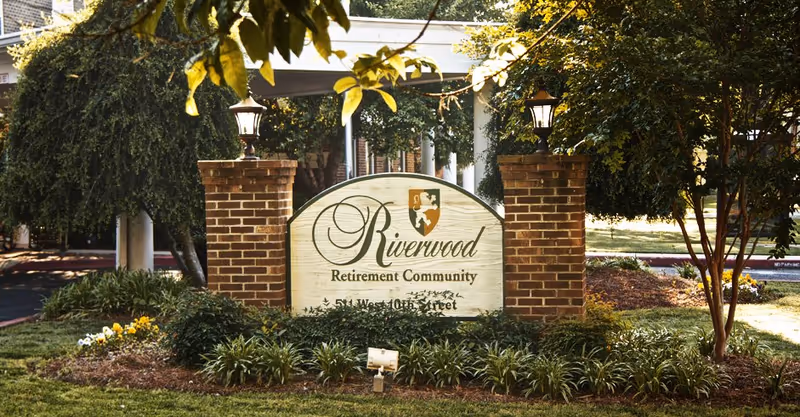 Riverwood Retirement Community entrance sign flanked by brick pillars and greenery.