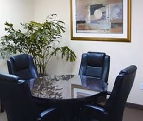 Small dining area with a glass round table, black chairs, plant, and framed art.
