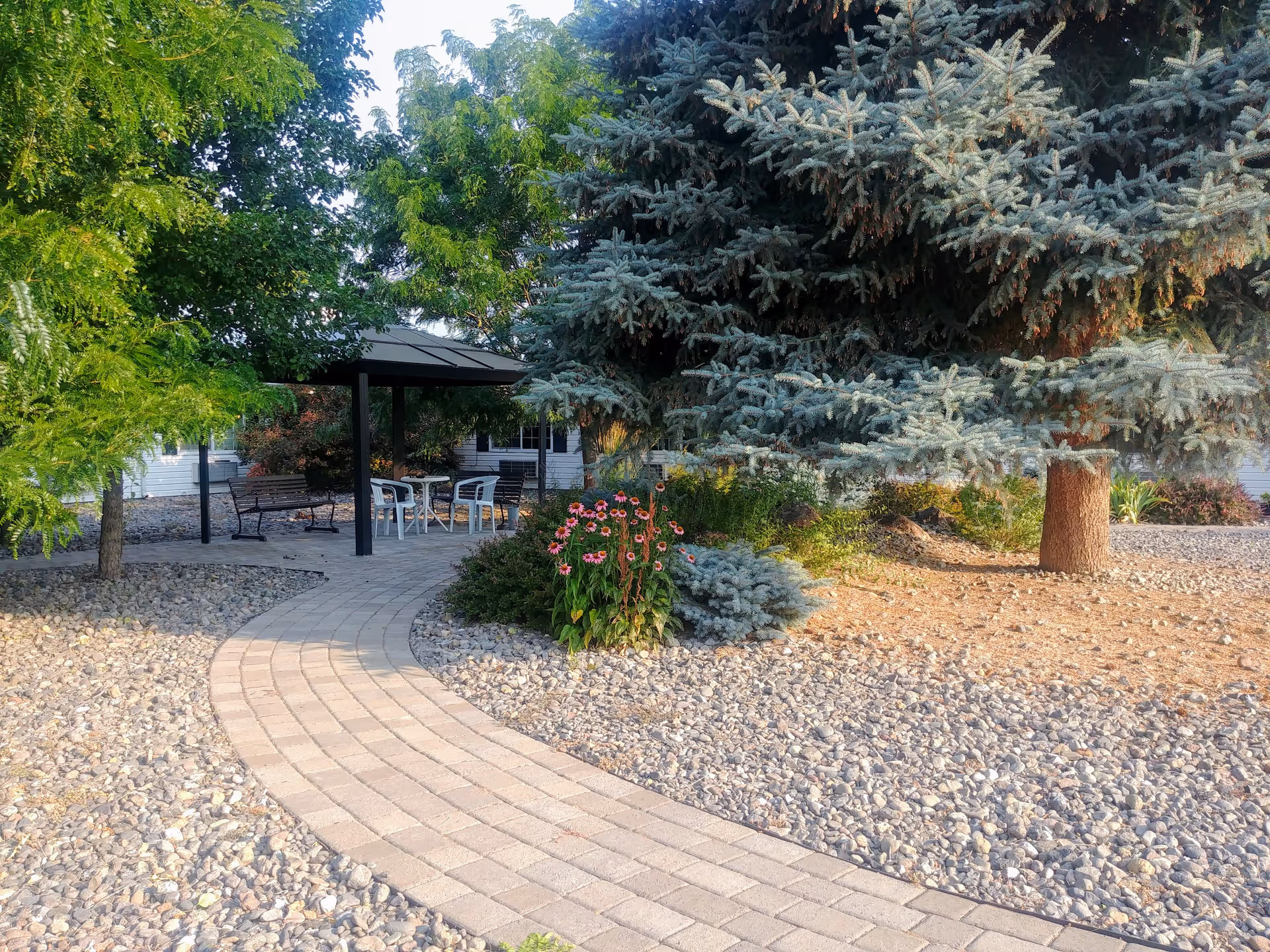 Stone pathway winds through a landscaped outdoor seating area with a gazebo and trees.