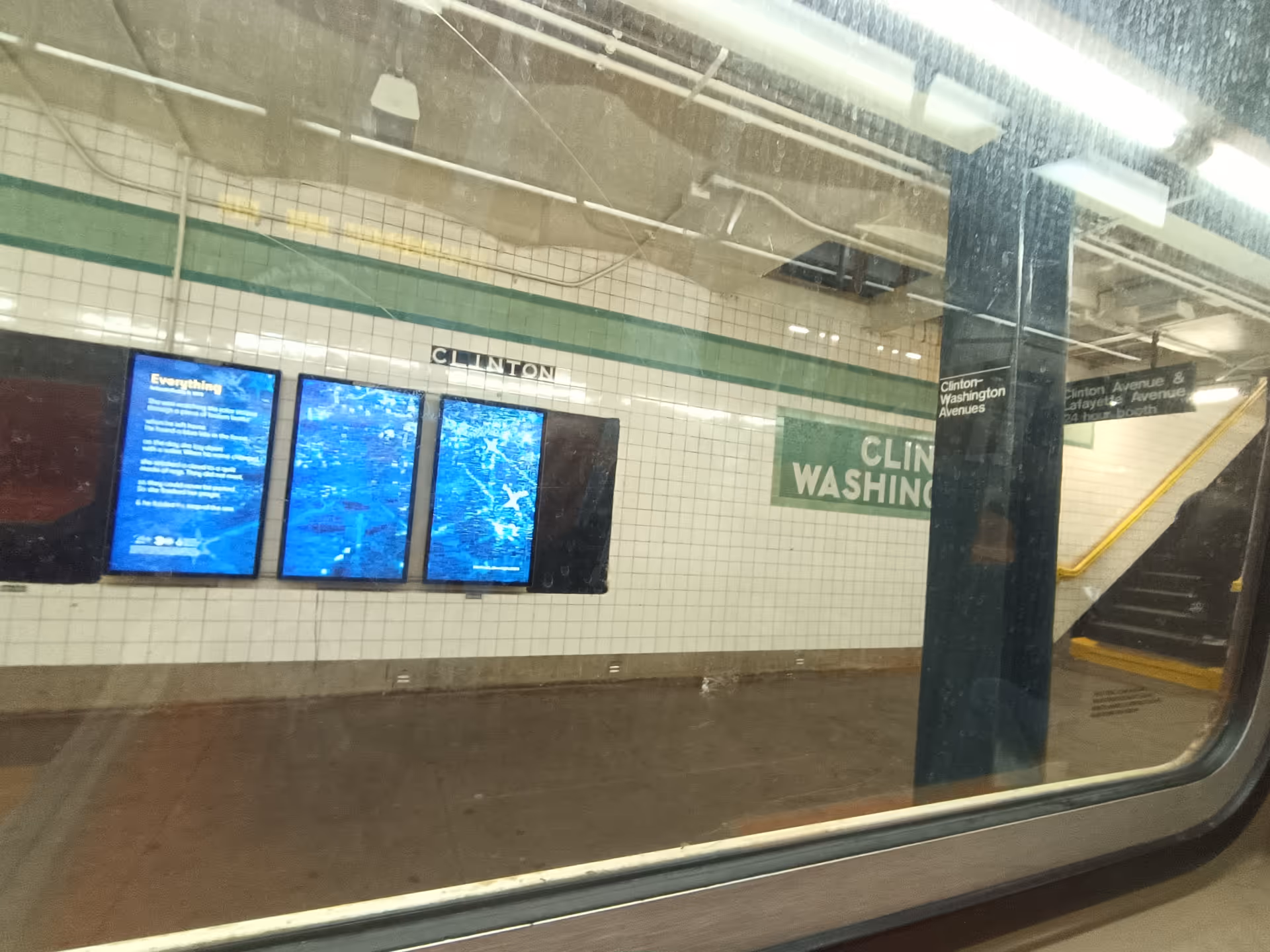 Subway platform with tiled walls, digital display boards, and a stairway.
