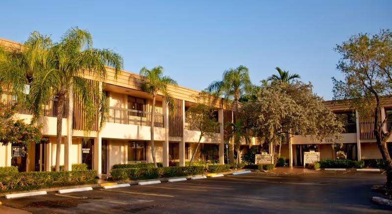 Two-story beige senior living building with palm trees and a parking lot exterior.