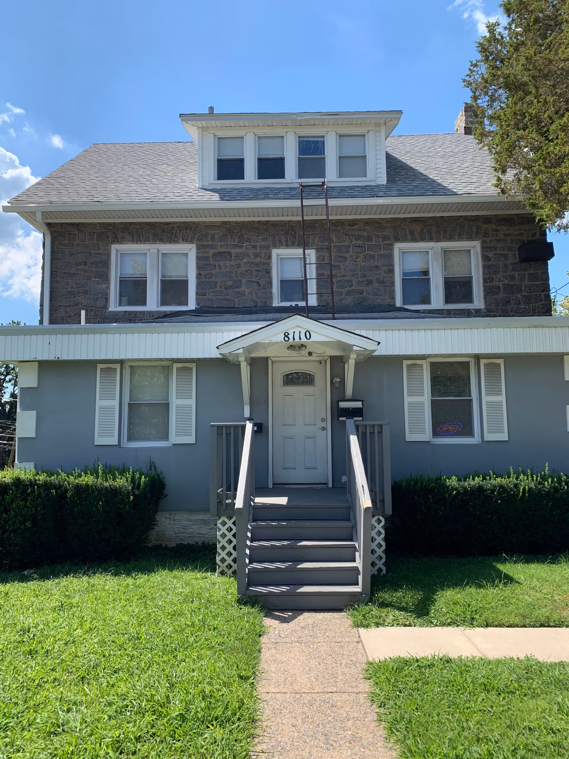 Two-story stone-and-siding facility with front stairs, a porch canopy, and a manicured lawn.