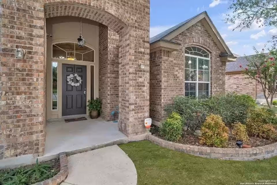 Brick residence with arched entry, front door, porch light, and manicured shrubs.