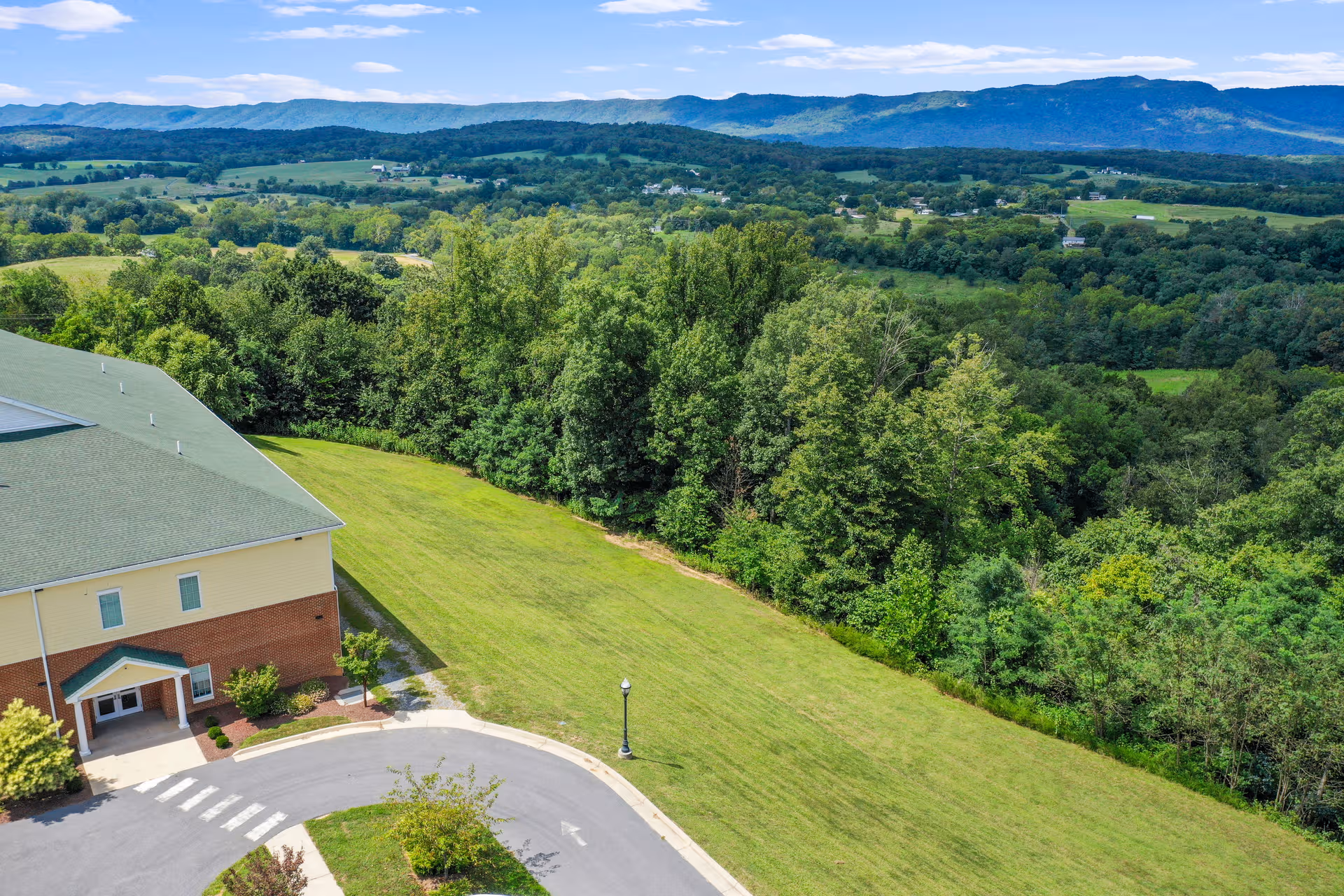 A senior living facility exterior with a curved driveway and green lawn leading to the entrance.