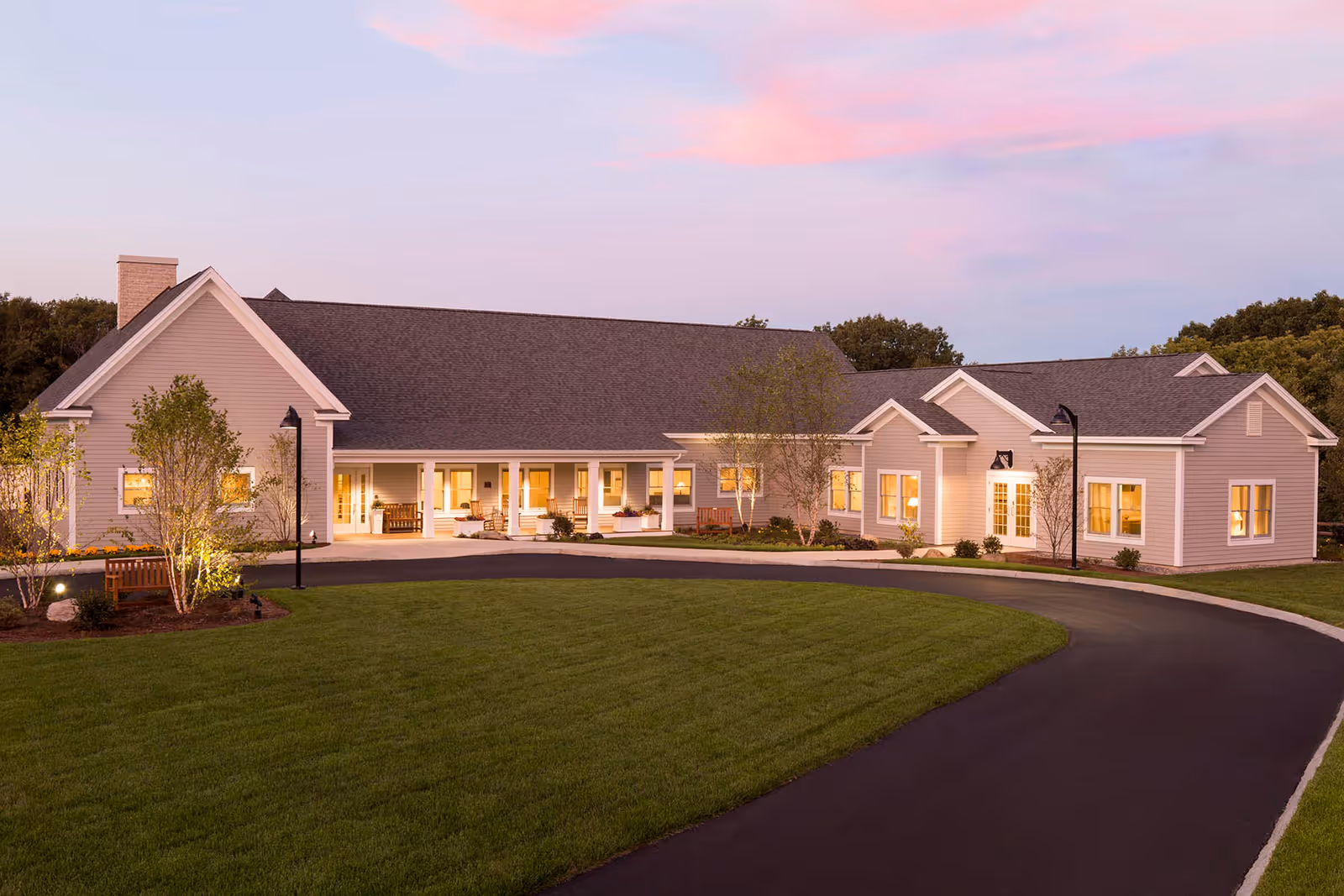 Single-story hospice facility with a curved driveway, beige siding, and warmly lit entrance at dusk.