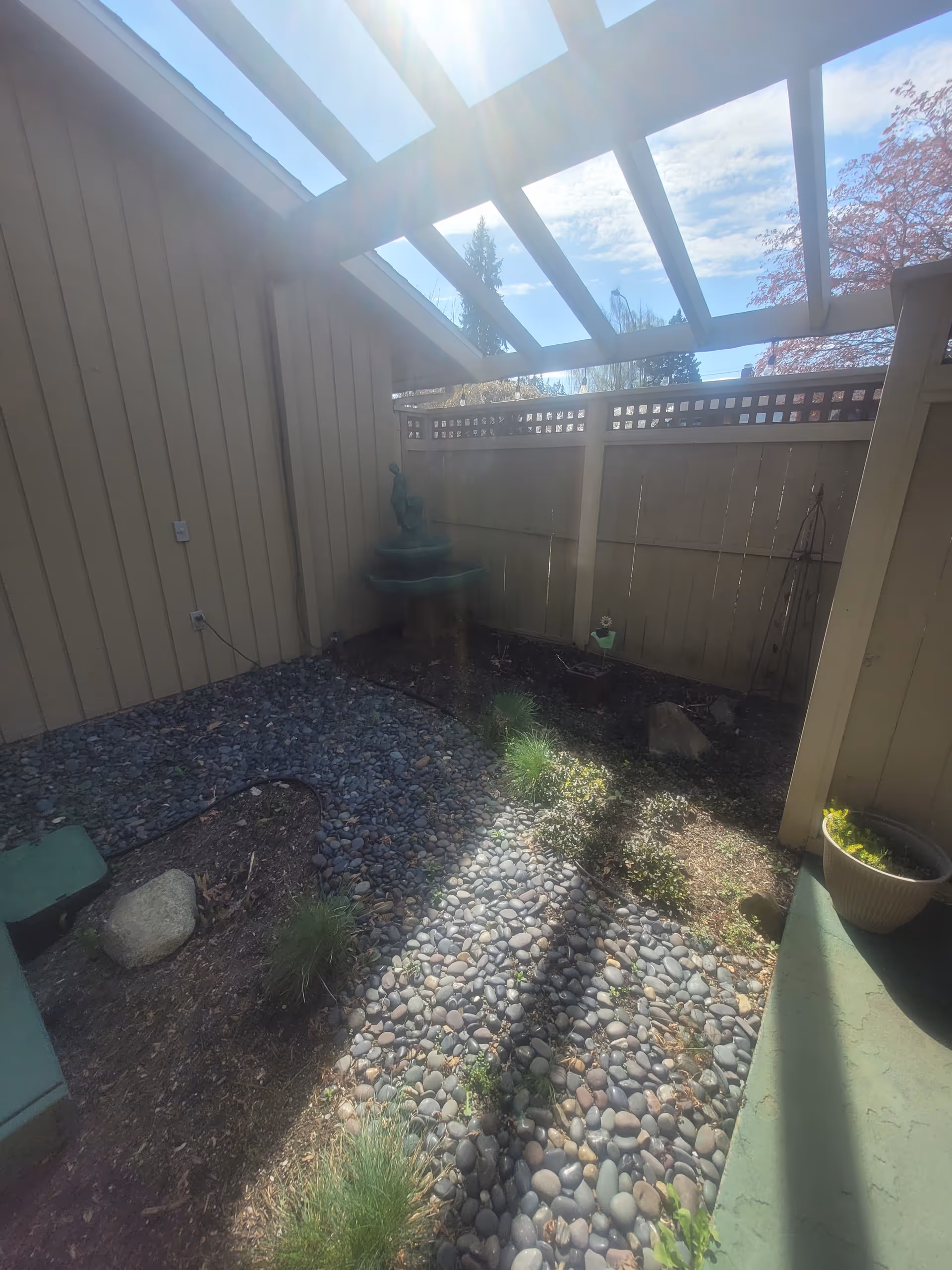 Enclosed outdoor courtyard with a stone path, fountain, gravel beds, and wood fence.