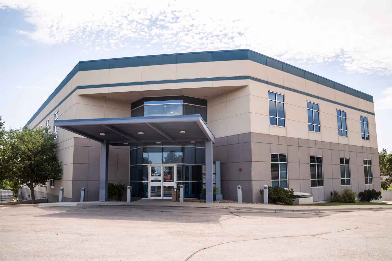 Modern two-story medical facility exterior with glass entrance and blue canopy