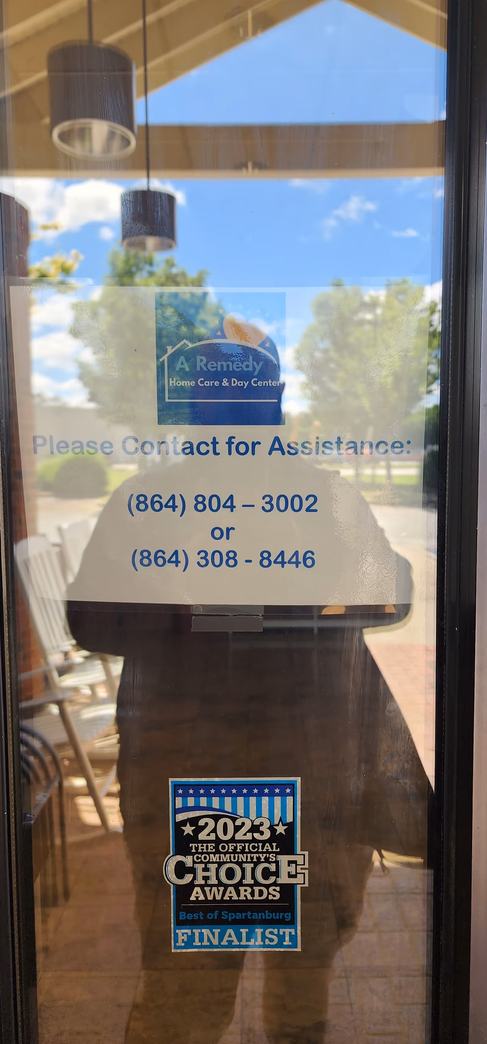 Glass door displays A Remedy Home Care and Day Center sign, contact numbers, and award sticker.