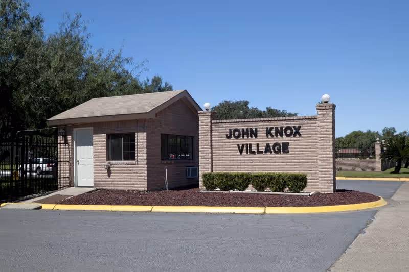 Exterior view of John Knox Village entrance with brick sign and trimmed landscaping.