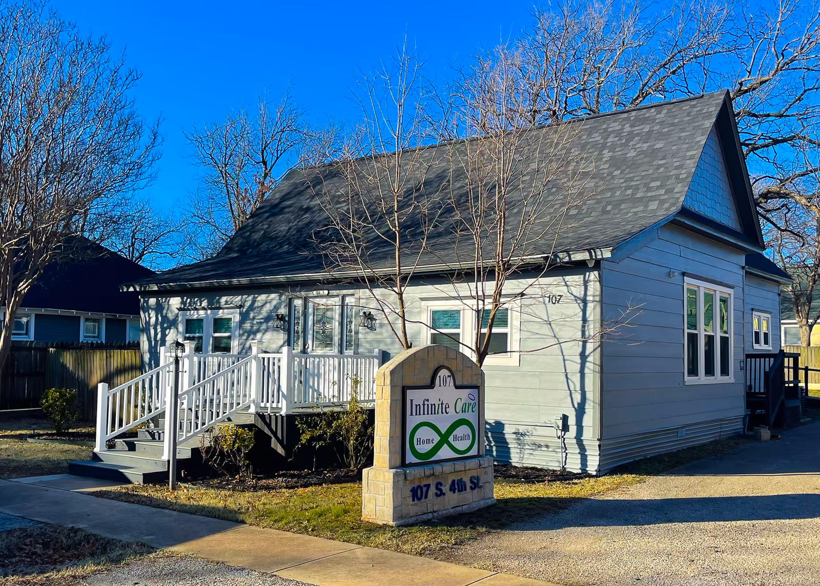 Blue bungalow-style care facility exterior with ramp, sign, and bare trees.