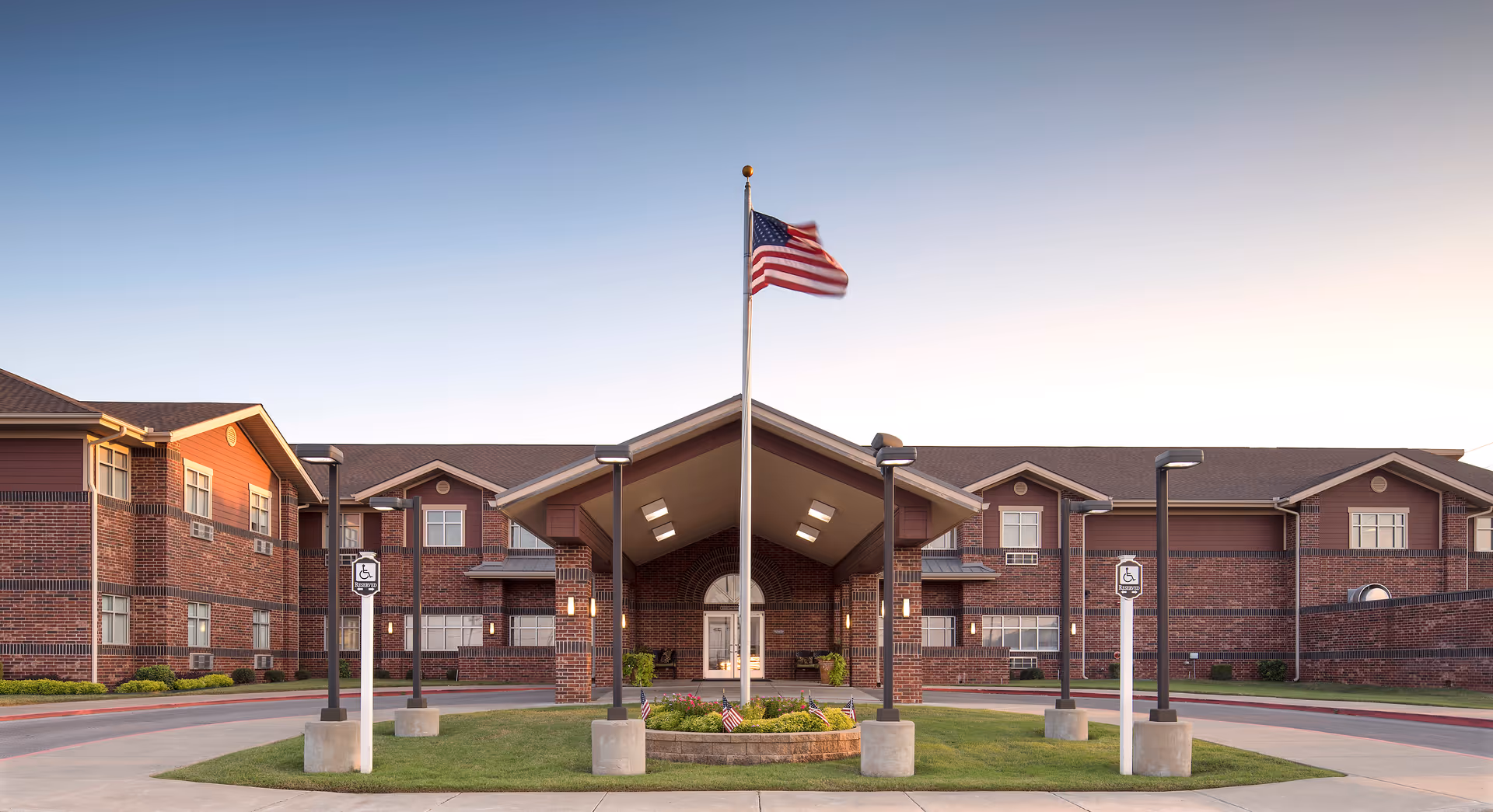 Brick assisted living facility with central porte-cochère and American flag at entrance.