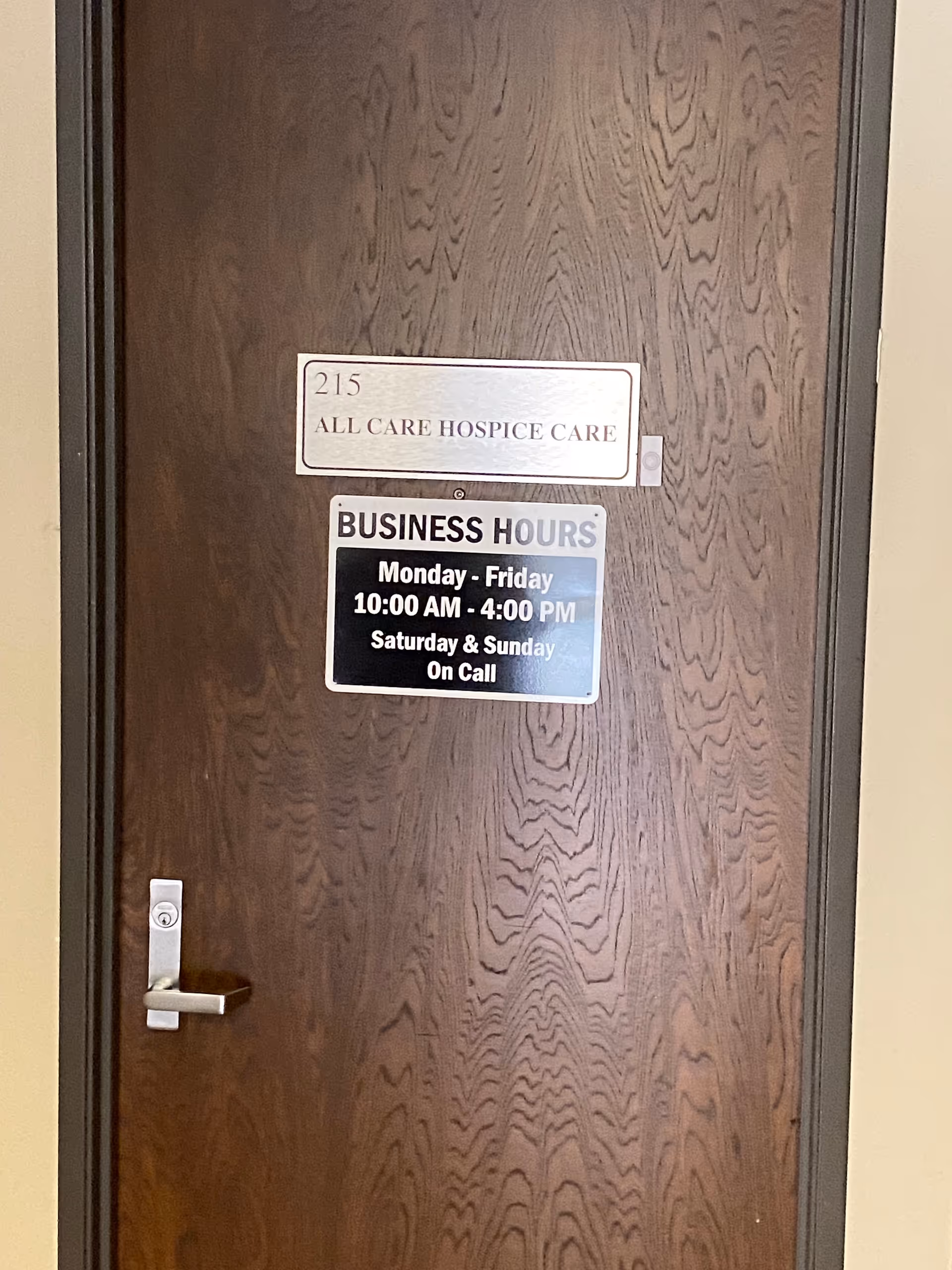 Wooden interior door displaying All Care Hospice Care and business hours signs.