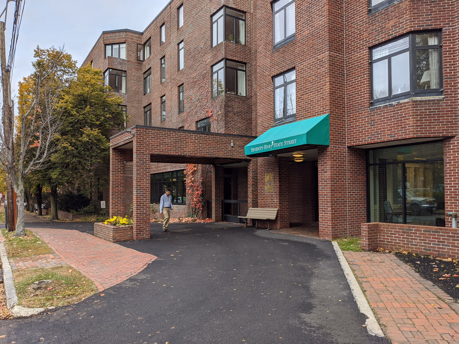 Brick senior living facility entrance with green awning and a person walking toward the entry.