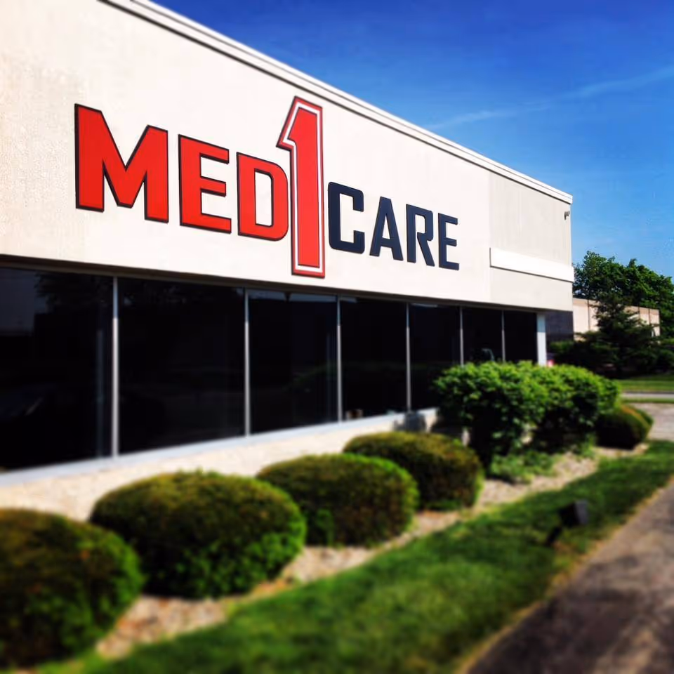 Exterior view of a Med1Care building with a large red and blue sign and landscaping.