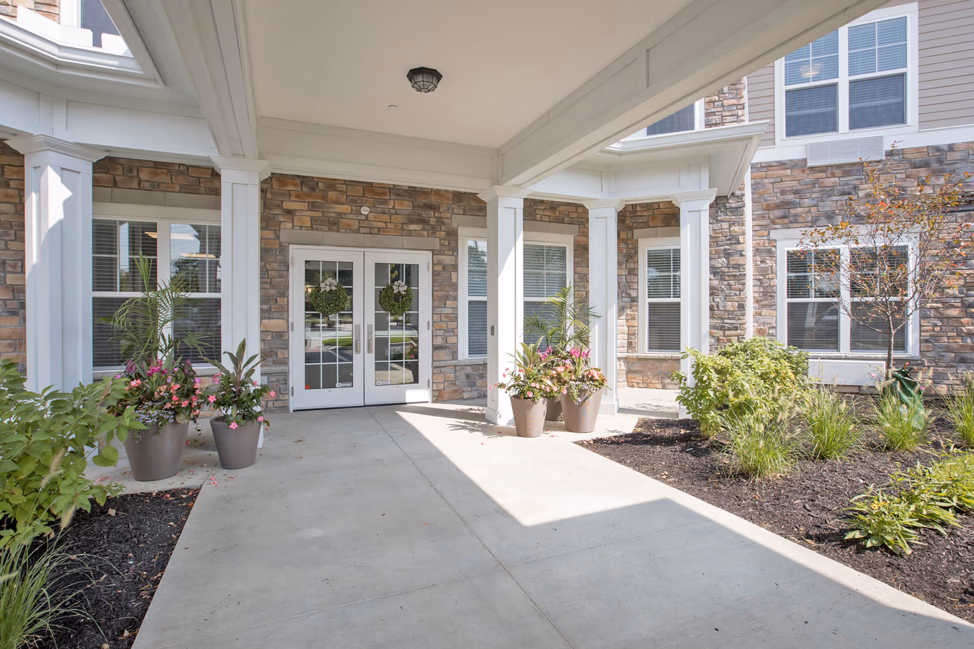 Stone facade building entrance with white columns, double doors, and potted plants.