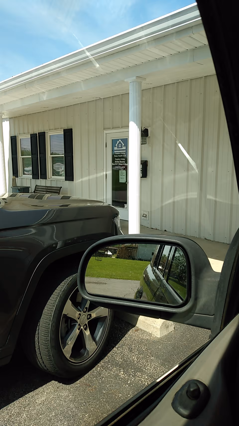 White facility exterior with front door, windows, a sign, and parked cars in foreground.