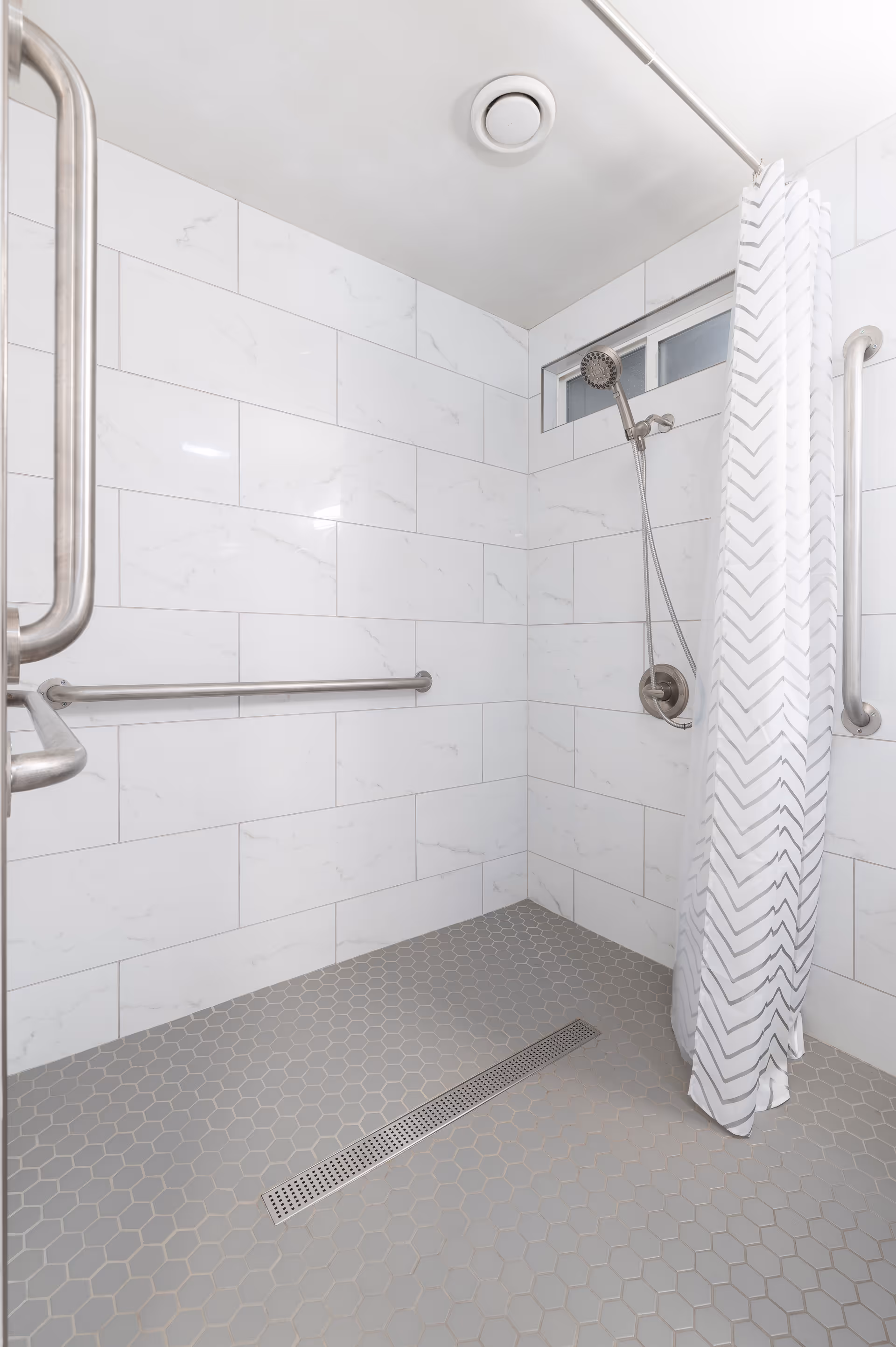 Accessible bathroom with tiled walls, a walk-in shower, curtain, and grab bars.