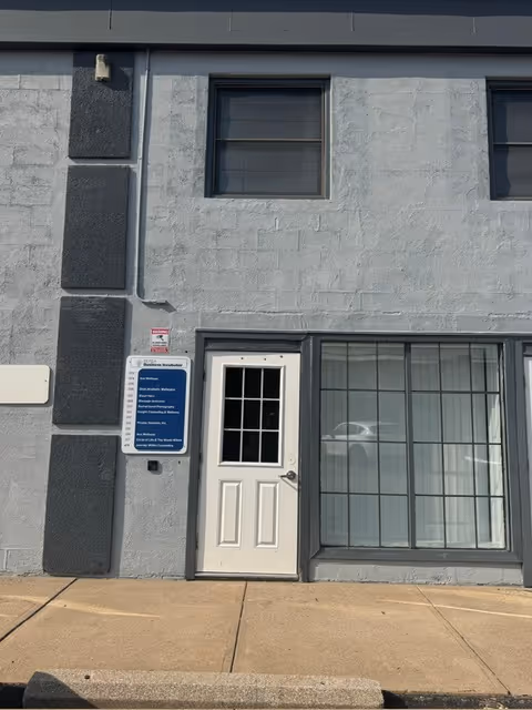 Grey building exterior with white door, large window, and a blue sign near entrance.