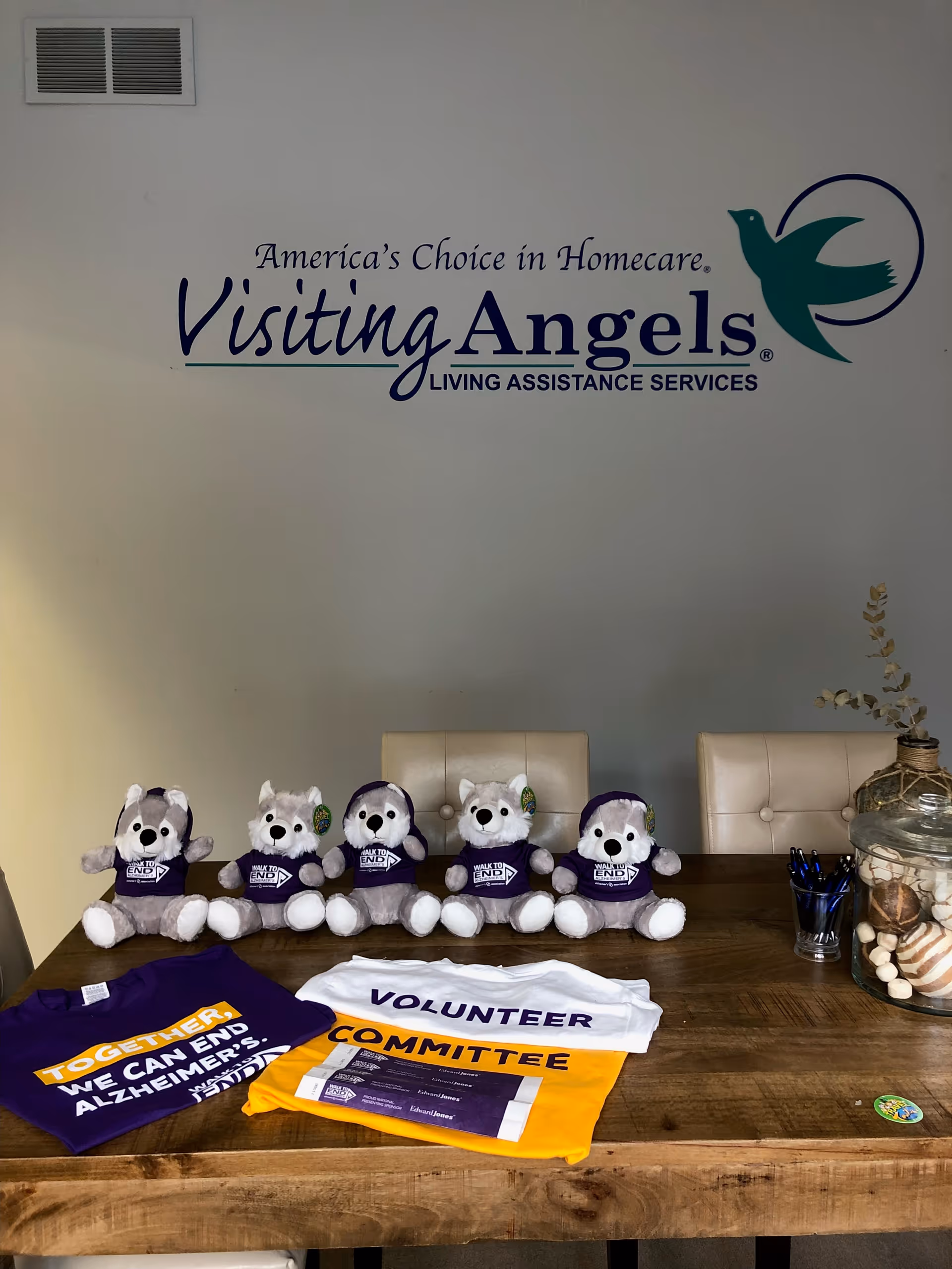 Interior wall featuring Visiting Angels logo and a table of plush bears and volunteer shirts.