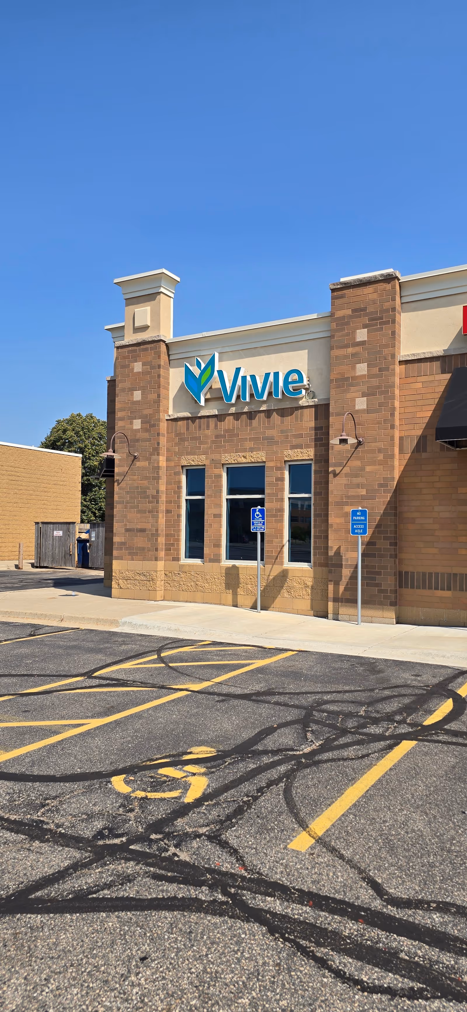 Brick building facade with a blue Vivie sign, handicap parking signs, and a clear blue sky.