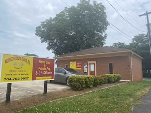 Exterior of a brick senior home care facility with a large yellow sign and parked car