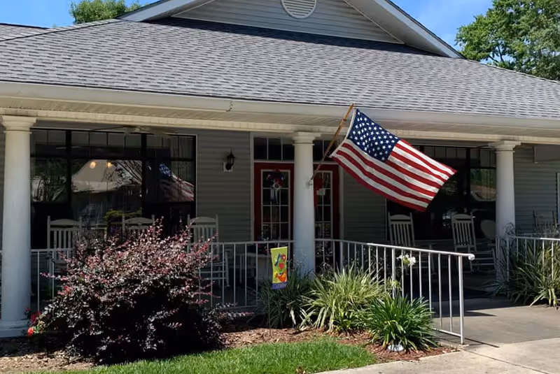 Front view of The Meadows of Atmore building with a porch, columns, and American flag.